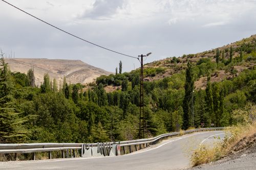 Free A winding road through lush green hills and trees under a partly cloudy sky in Elazığ, Türkiye. Stock Photo