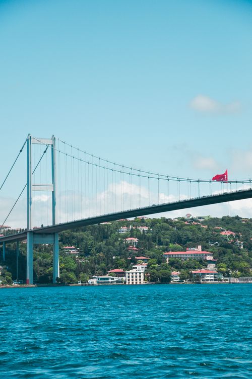 Free View of Bosphorus Bridge spanning across vibrant blue waters near a lush cityscape, featuring vivid skies. Stock Photo