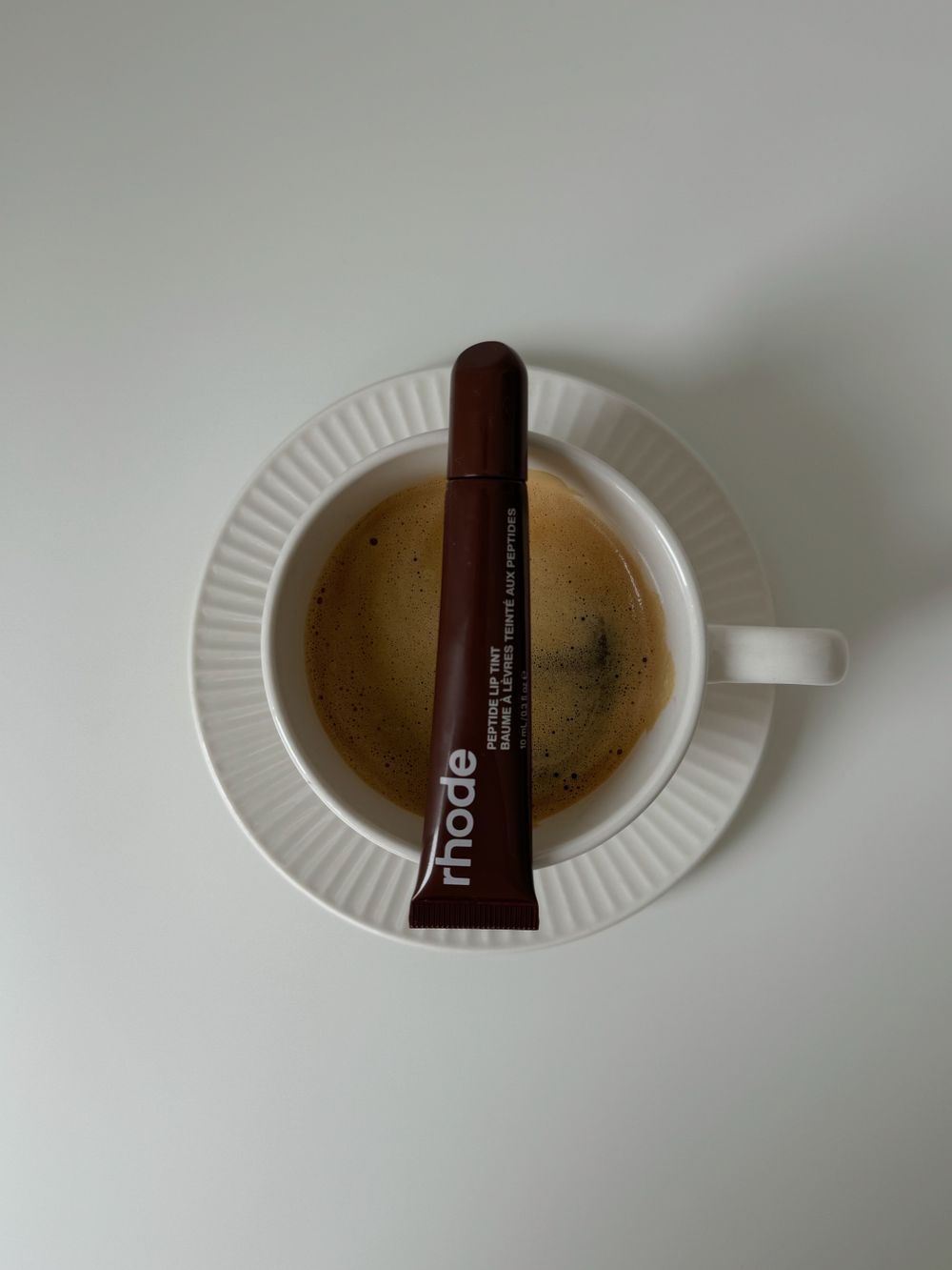 コーヒーカップとチューブ型リップ製品の静物写真