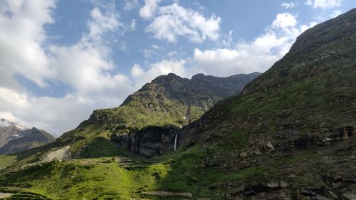 Free Breathtaking view of green mountains under a blue sky with a flowing waterfall. Stock Photo