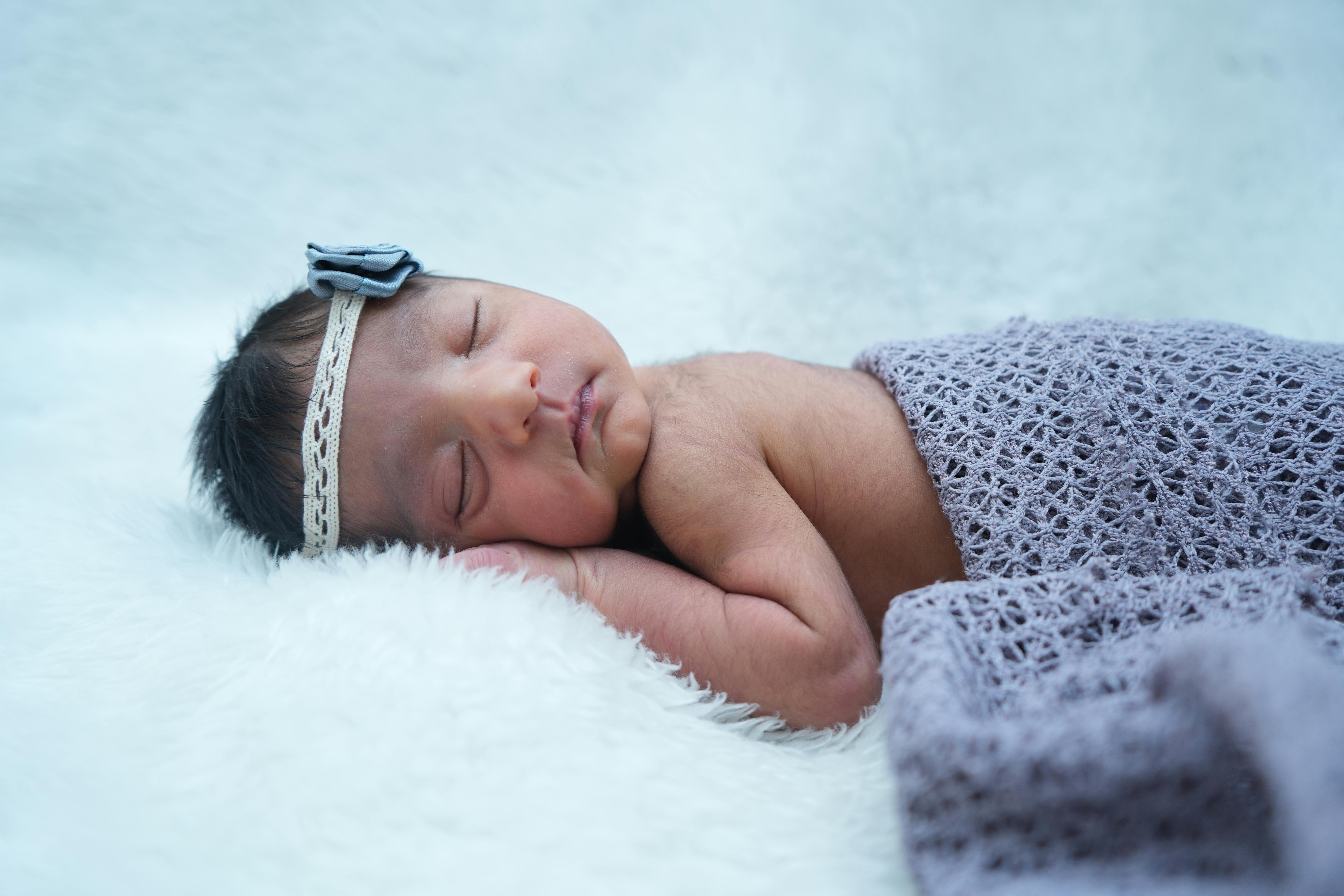 Close-up of a newborn baby sleeping peacefully on a soft surface with a blue headband.