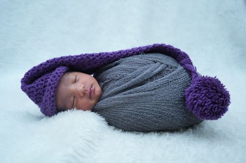 Free Adorable newborn baby sleeping wrapped in gray and purple blanket and hat on soft background. Stock Photo