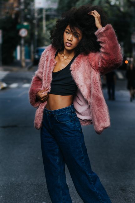 Fashionable woman with afro posing in urban street wearing a stylish pink fleece coat and jeans.
