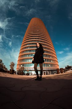 Low angle view of a woman standing in front of a modern skyscraper in Sevilla, Spain.