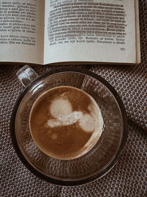 Free A warm cup of coffee beside an open book on a textured surface inviting relaxation. Stock Photo