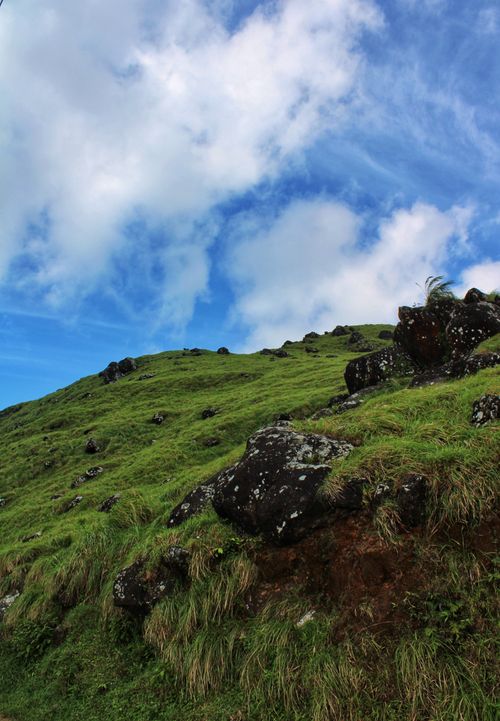 Free A picturesque green hillside with scattered rocks under a vibrant blue sky and fluffy clouds. Stock Photo