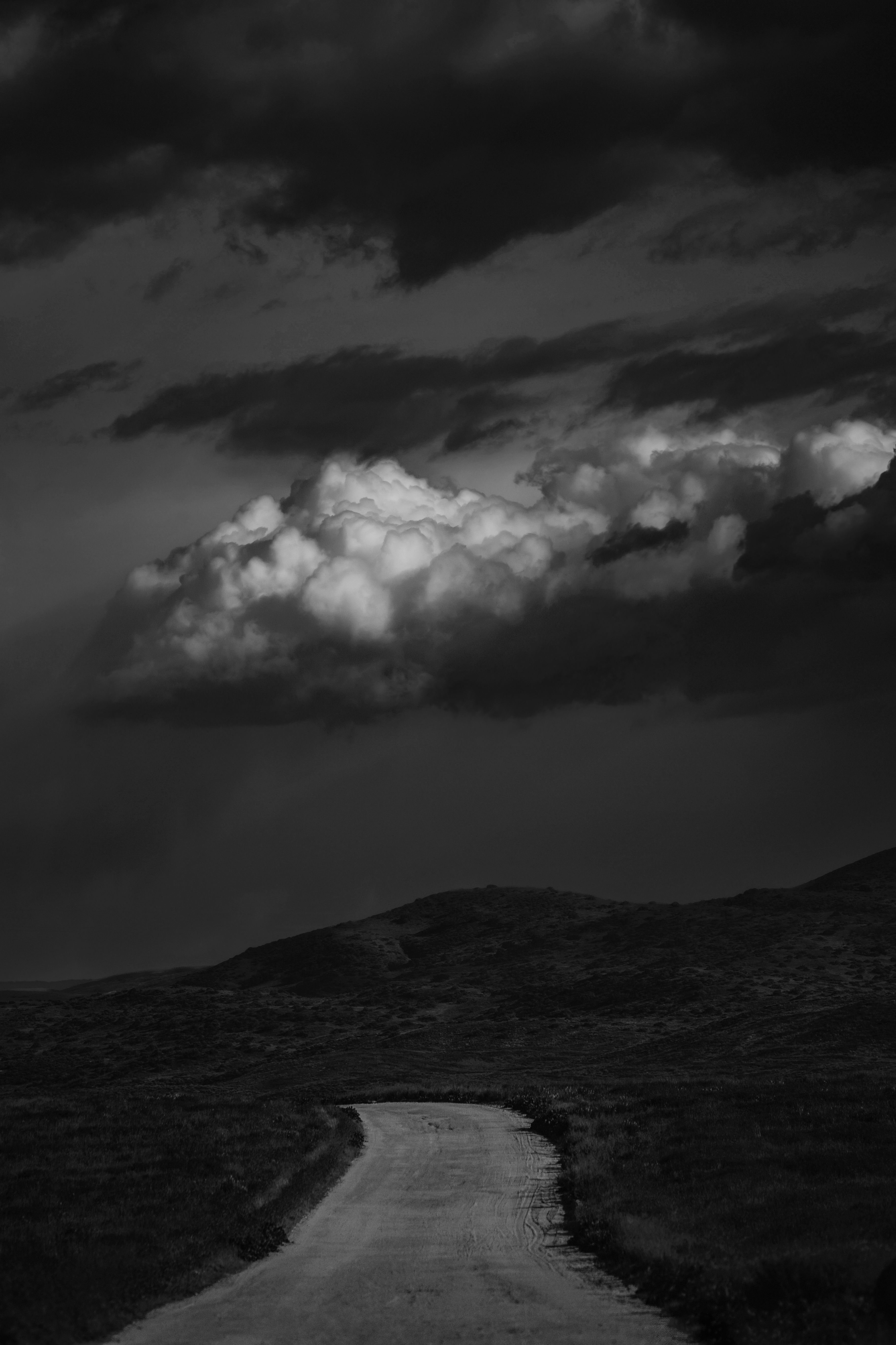A dramatic black and white image of a rural road leading into dark, cloudy skies.