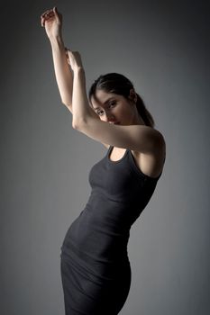 Woman in black dress striking a dramatic pose against a neutral backdrop.