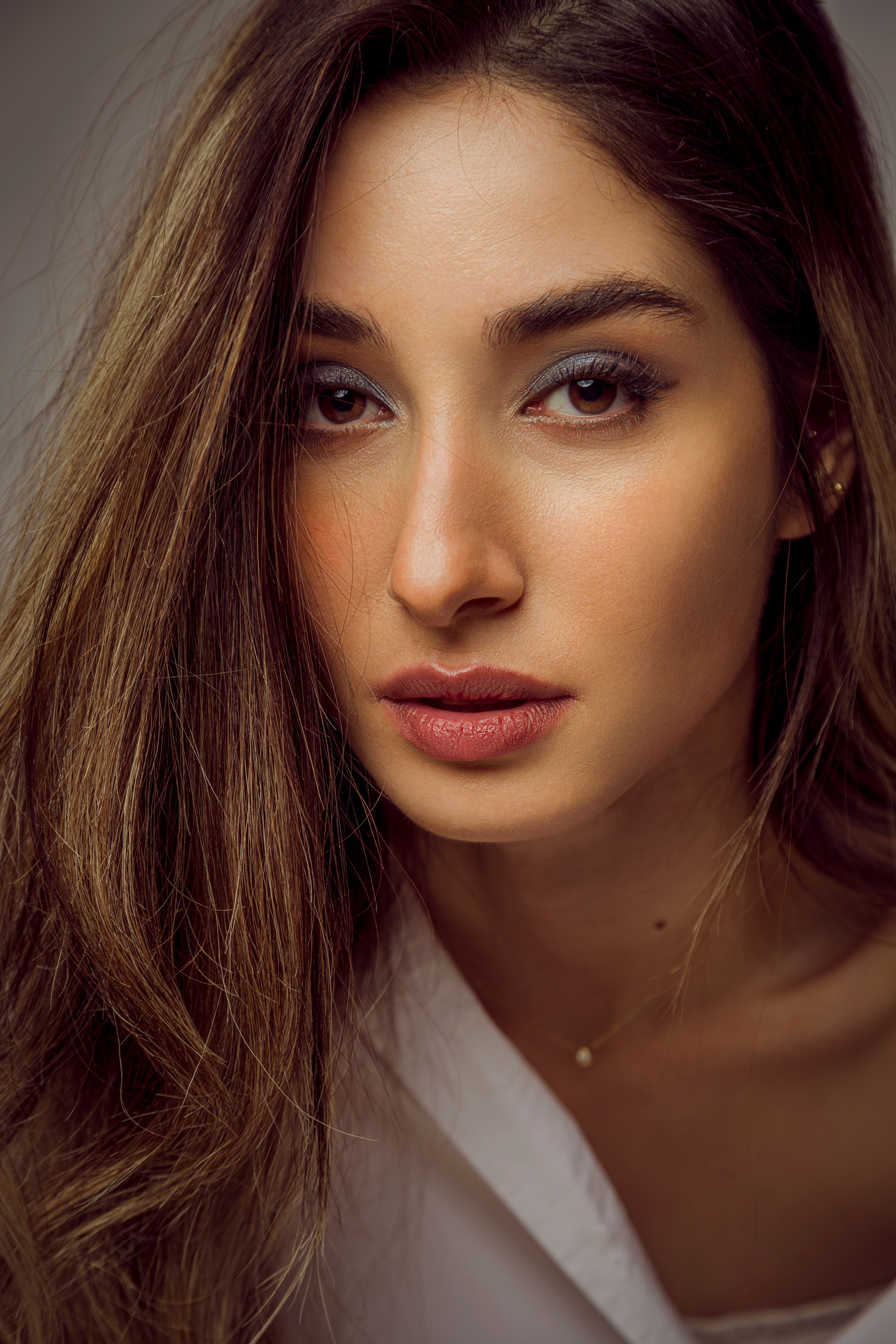 Close-up portrait of an elegant woman with long brown hair and neutral expression.