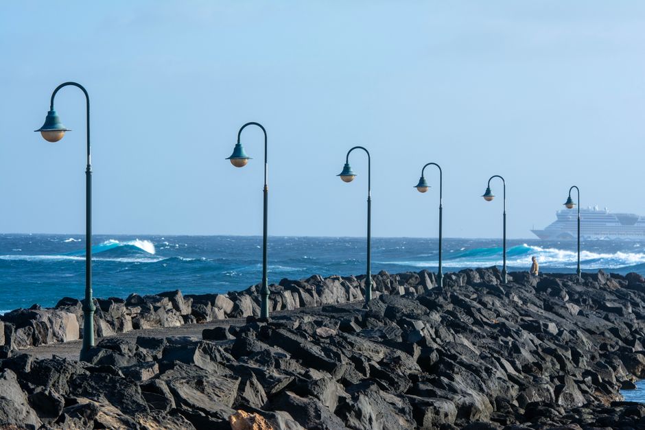 Beautiful ocean pier with lampposts and waves, featuring a distant cruise ship.