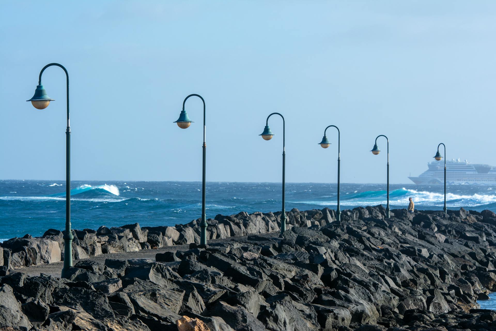 Beautiful ocean pier with lampposts and waves, featuring a distant cruise ship.