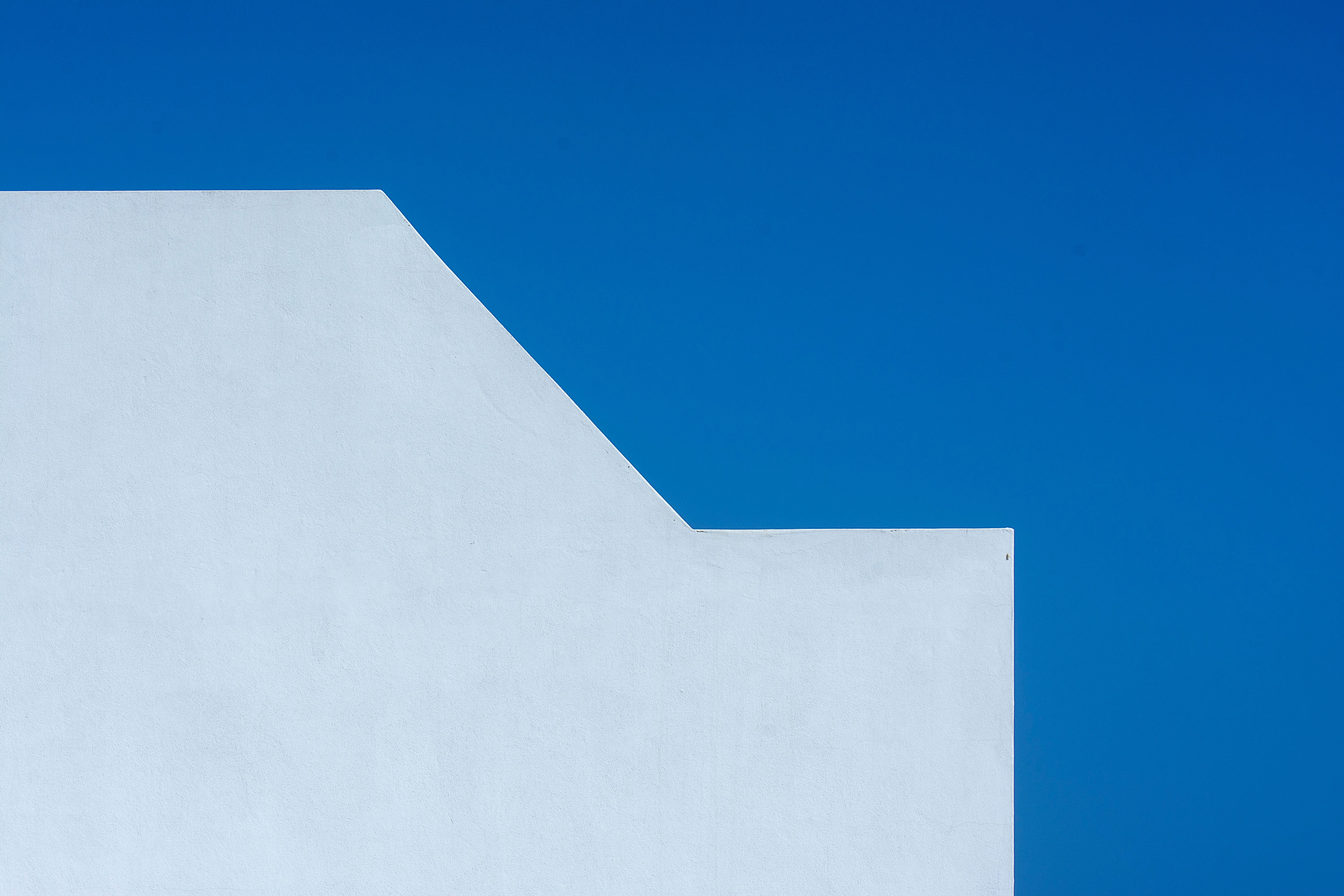 A minimalist photo of a white wall contrasting with a vibrant blue sky, showing geometric simplicity.