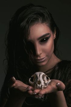 Dark, artistic portrait of a woman with dramatic makeup holding a skull, creating a mysterious mood.