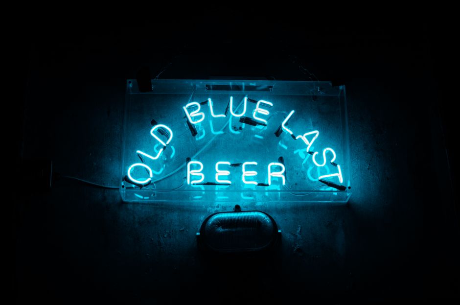 A bright blue neon sign reading 'Old Blue Last Beer' glowing in the dark.