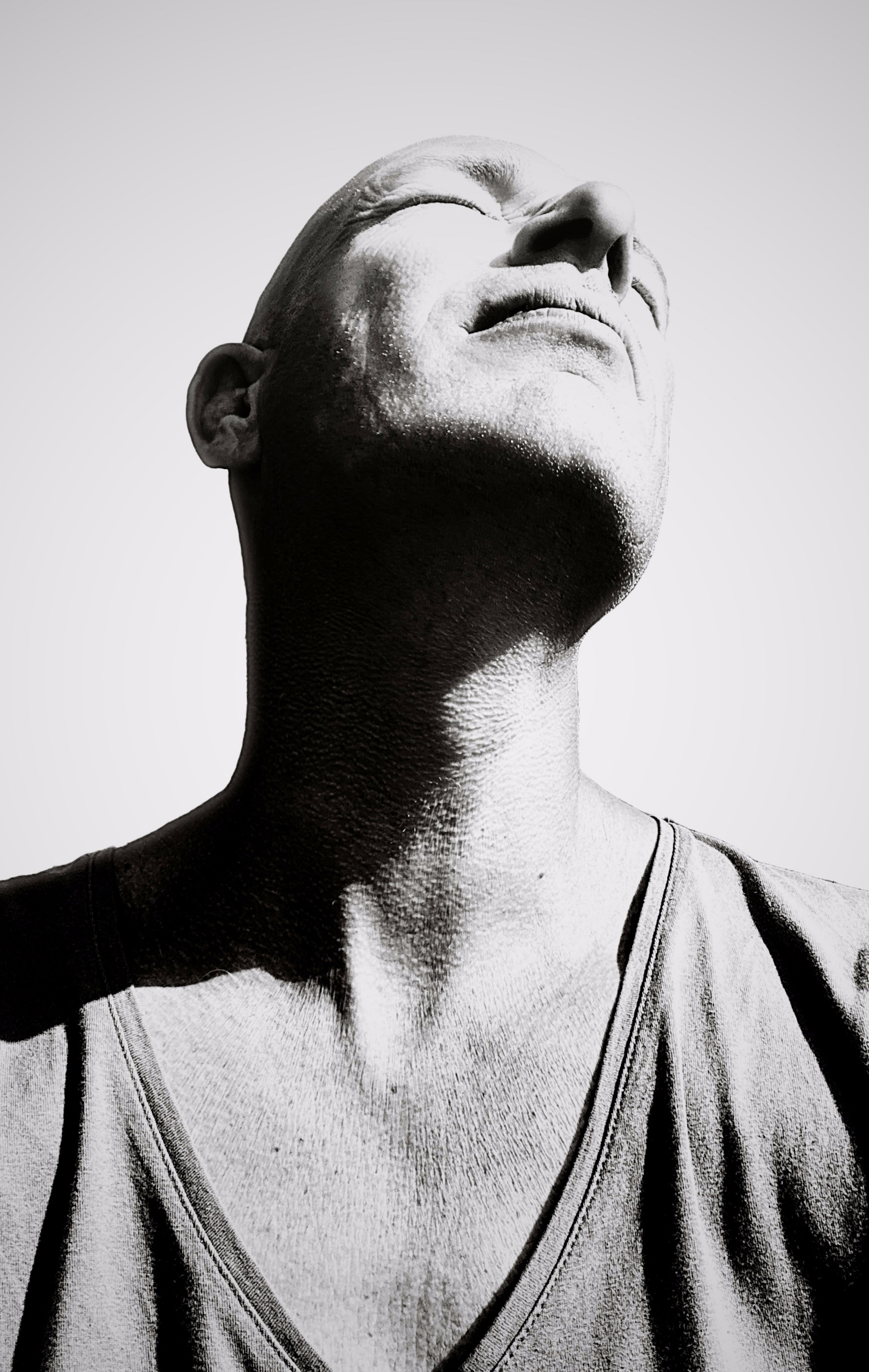 Black and white portrait of a man looking upward, basking in sunlight.