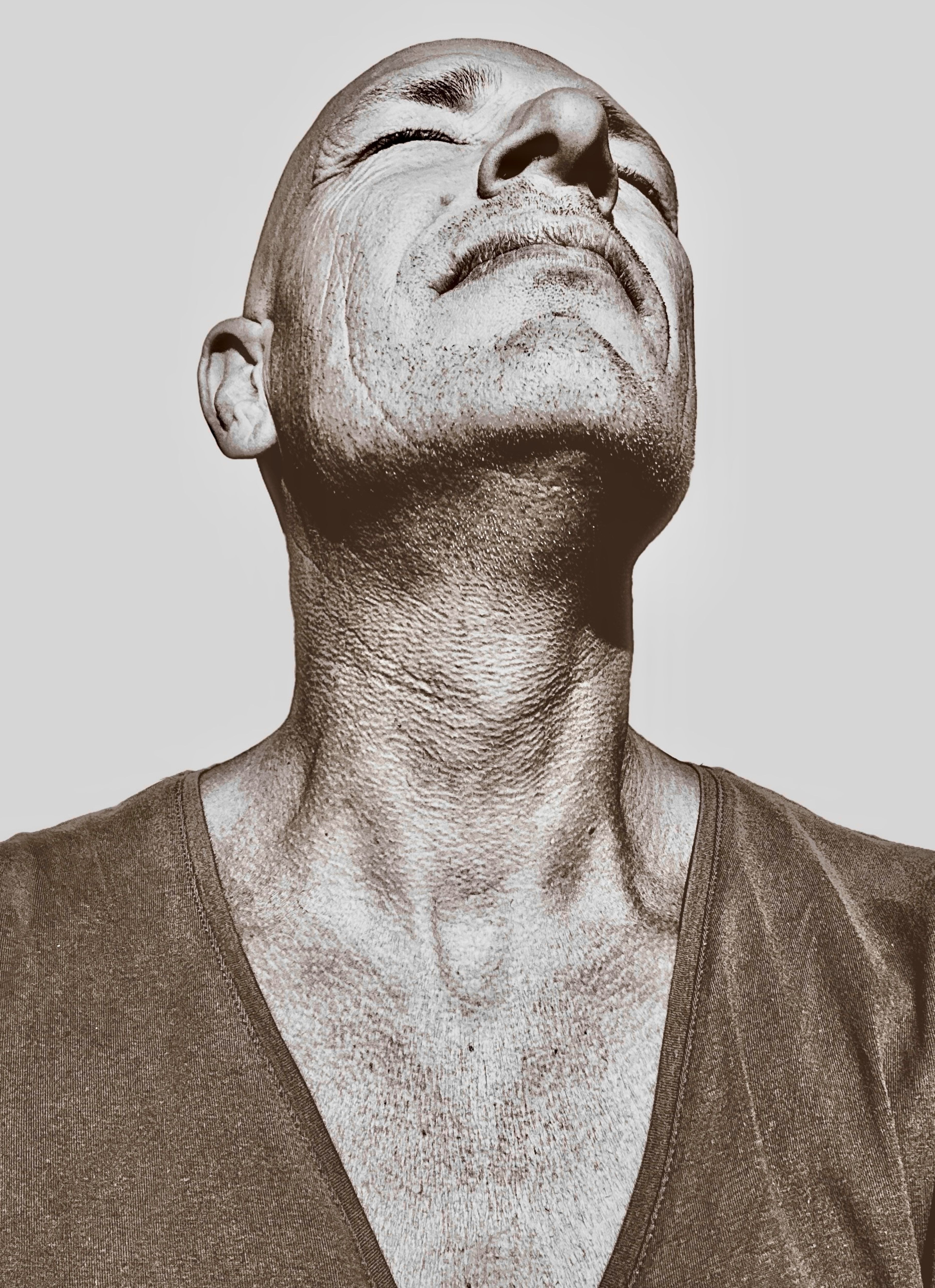 A powerful sepia-toned portrait of a middle-aged bald man gazing upwards. Emotion and strength captured.