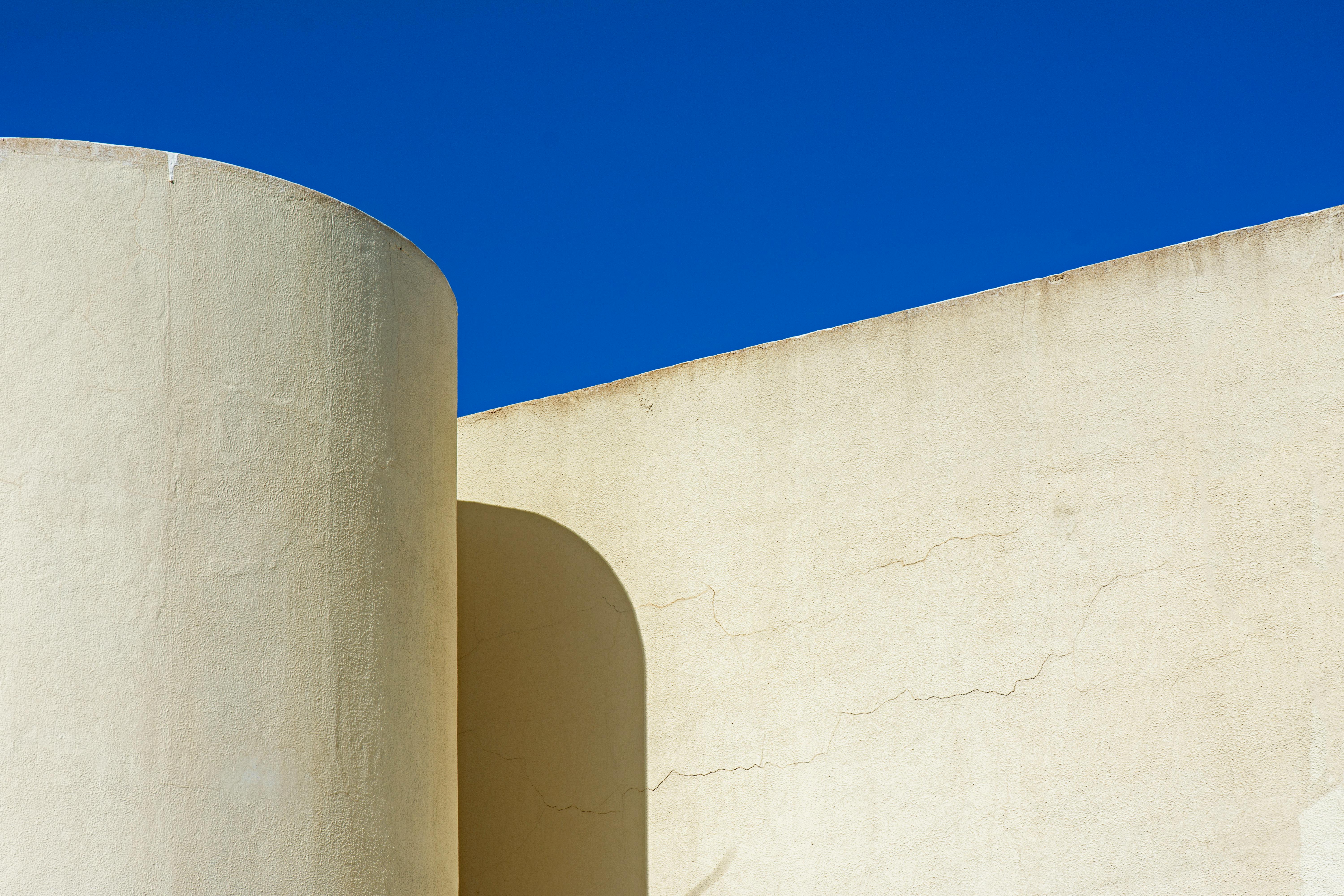 Minimalist architecture featuring beige walls with prominent shadows against a bright blue sky.