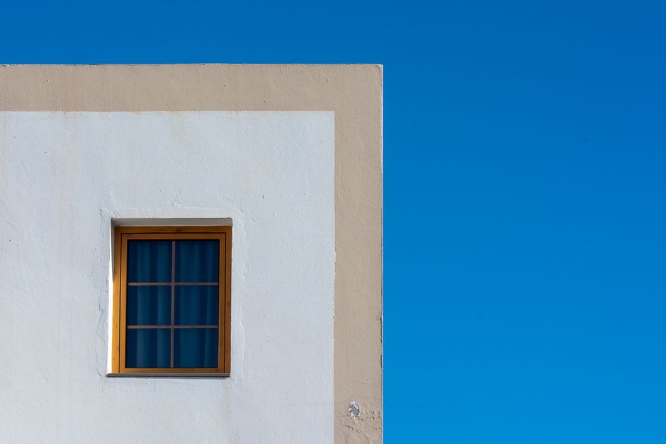A minimalist architectural facade featuring a window on a white wall contrasting with a clear blue sky.