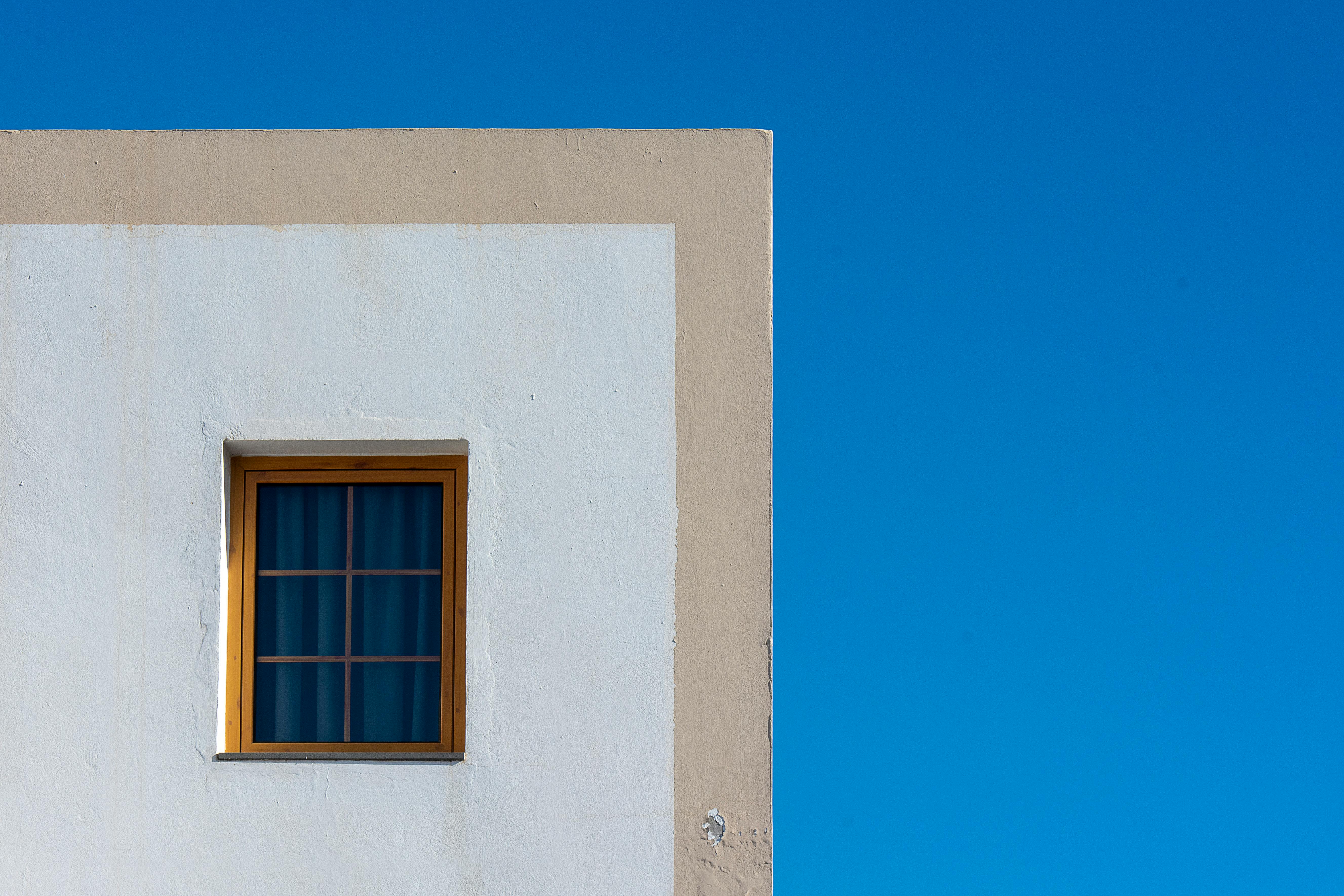 Free A minimalist architectural facade featuring a window on a white wall contrasting with a clear blue sky. Stock Photo