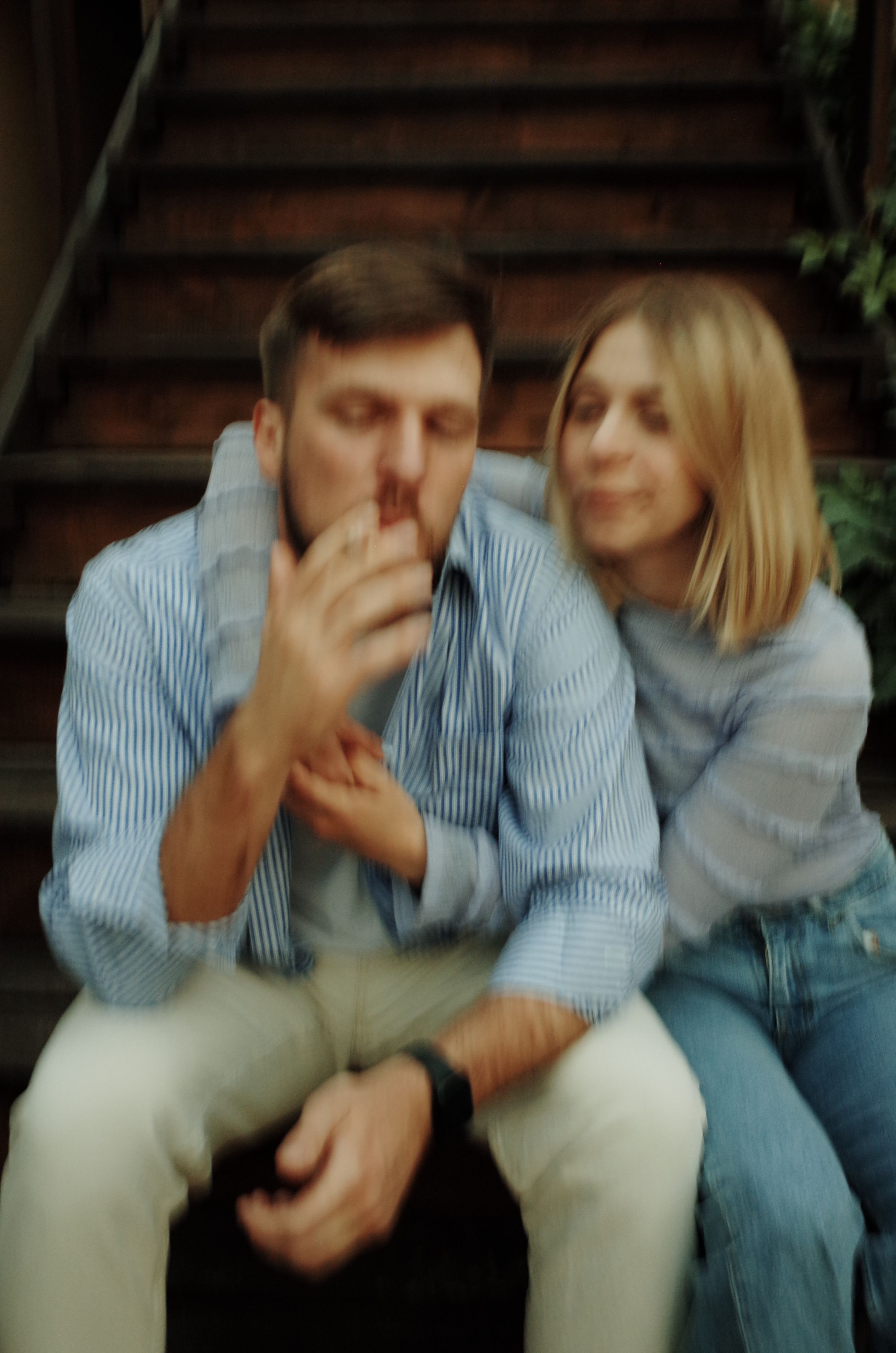 Blurry image of a couple sitting on outdoor stairs in casual attire.