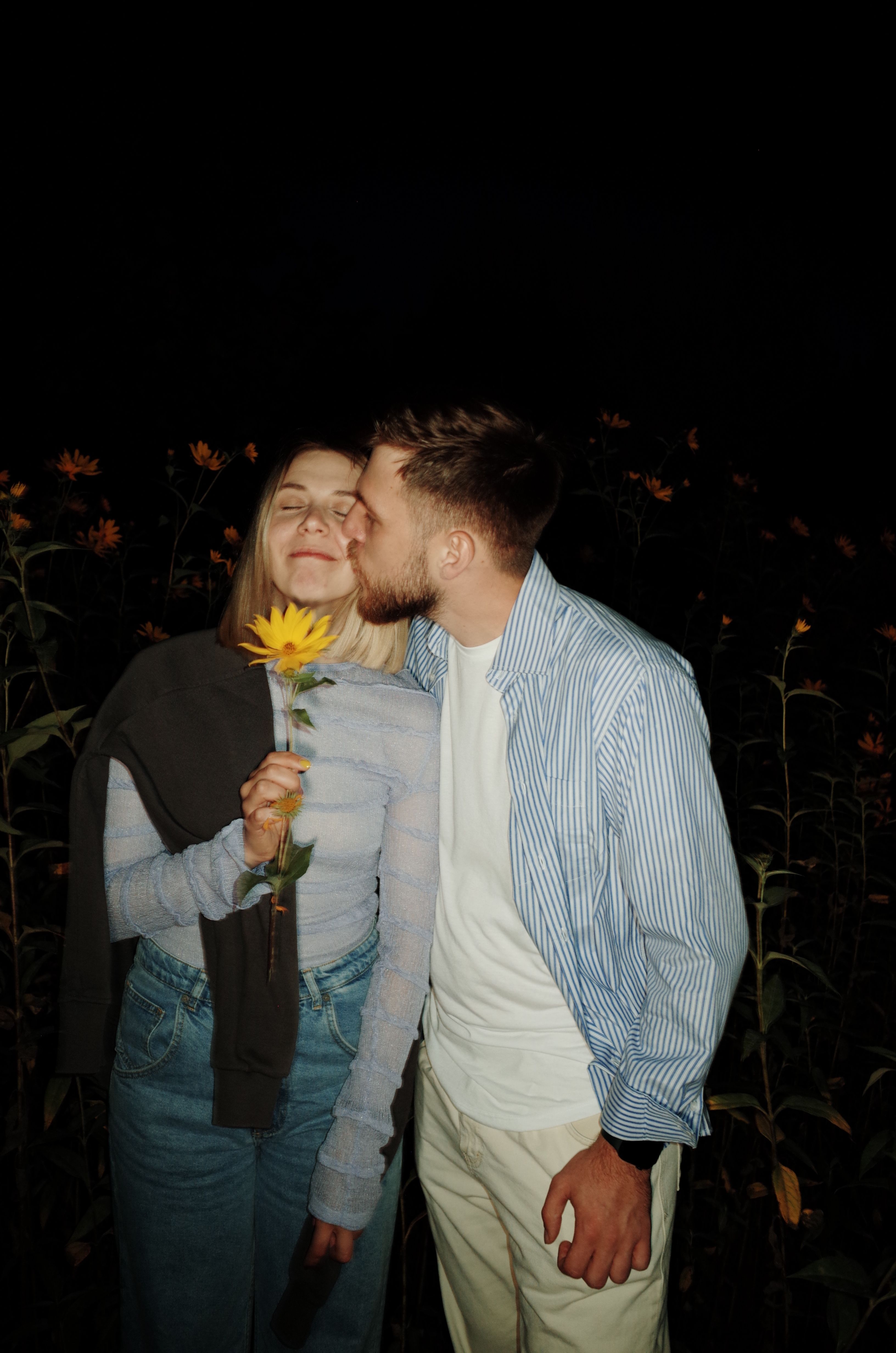A loving couple shares a romantic moment in a sunflower field at night.