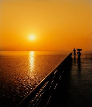 Experience the serene beauty of a golden sunrise over the ocean with silhouetted figures.