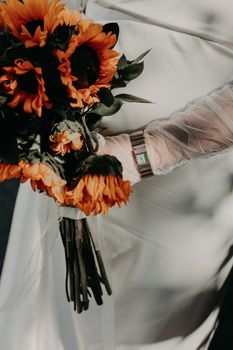 Bride in wedding dress holding a vibrant sunflower bouquet with a delicate lace sleeve.