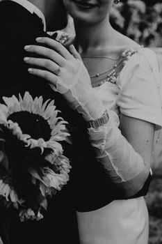 Artistic black and white photo of bride with elegant gloves holding sunflower bouquet.