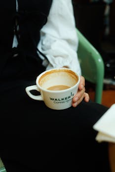 Person holding Walker's Coffee House cup with coffee indoors