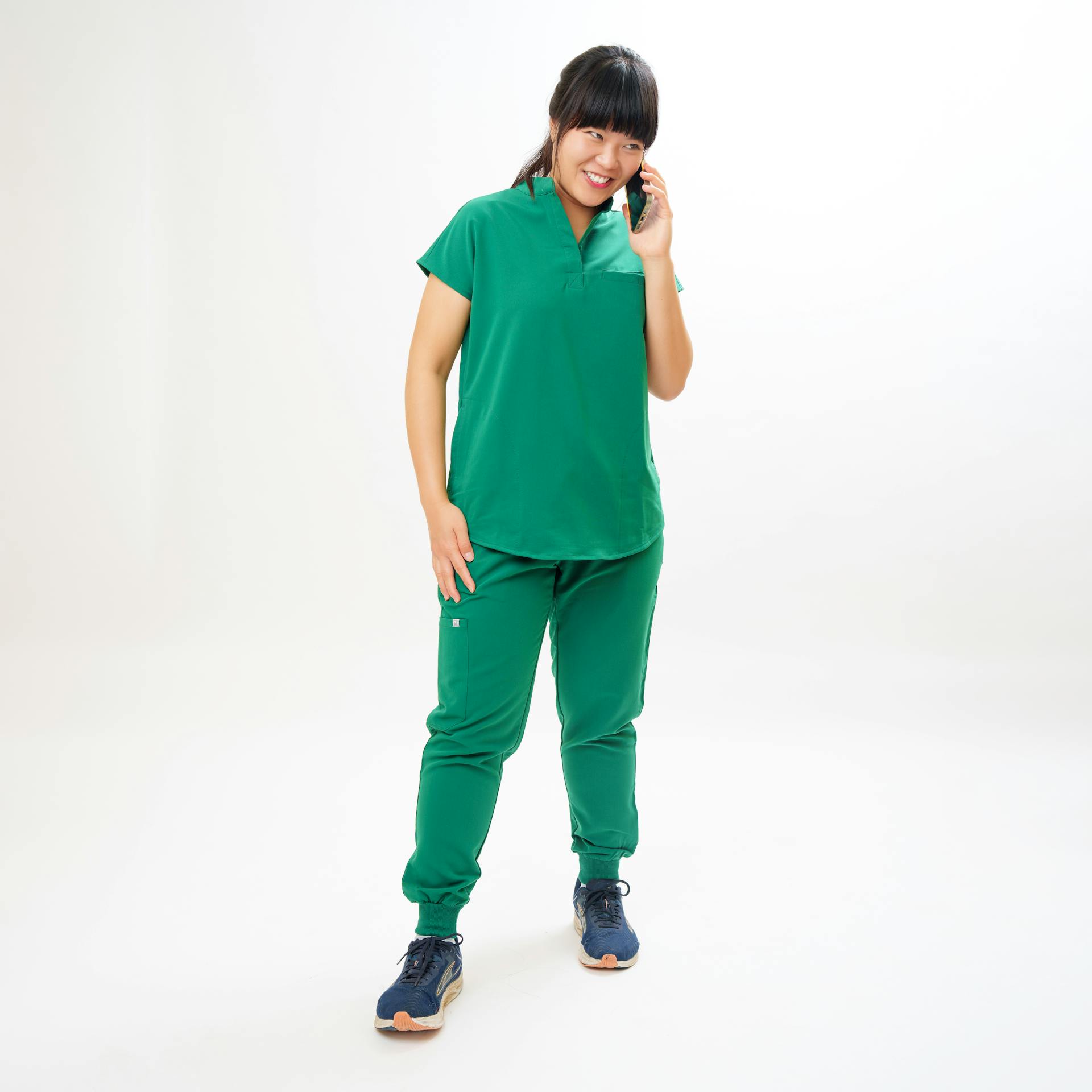 Female healthcare worker in green scrubs talking on phone, smiling.