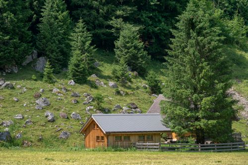 Free A serene wooden cabin surrounded by dense green forest and rocky terrain, perfect for nature retreats. Stock Photo