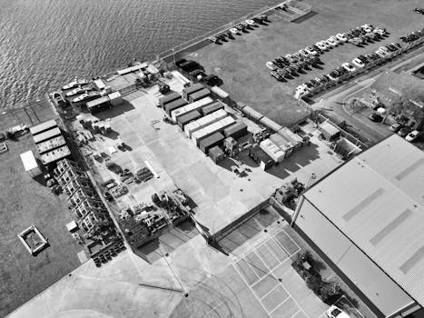 Monochrome aerial photo of an industrial yard near a waterfront with parked containers and vehicles.
