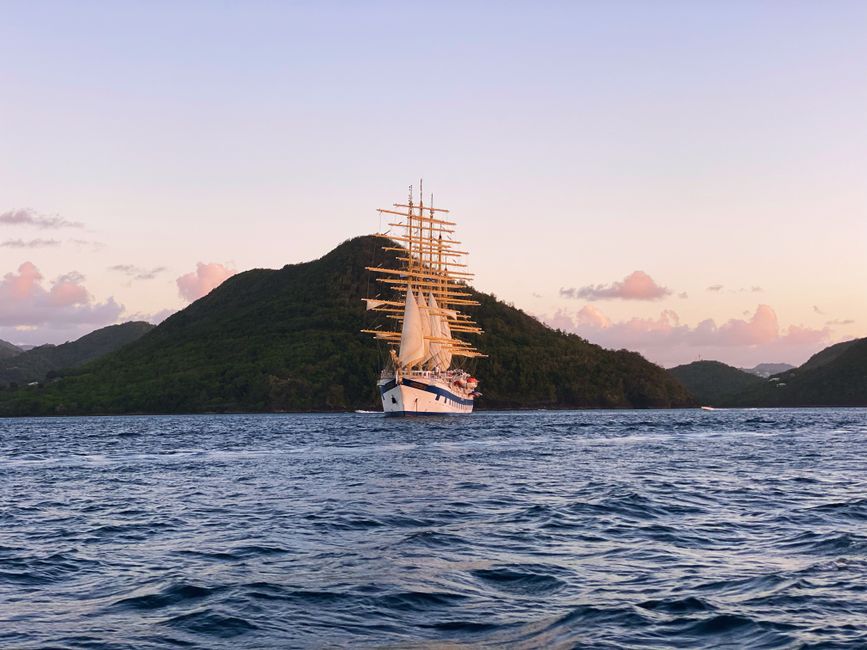 Majestic sailing ship navigating near a lush green island at sunset.