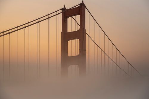 Free Iconic view of the Golden Gate Bridge emerging from fog at sunrise, casting a warm glow. Stock Photo