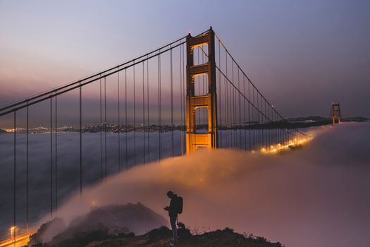 Silhouette of a person near the Golden Gate Bridge enveloped in dusk fog.
