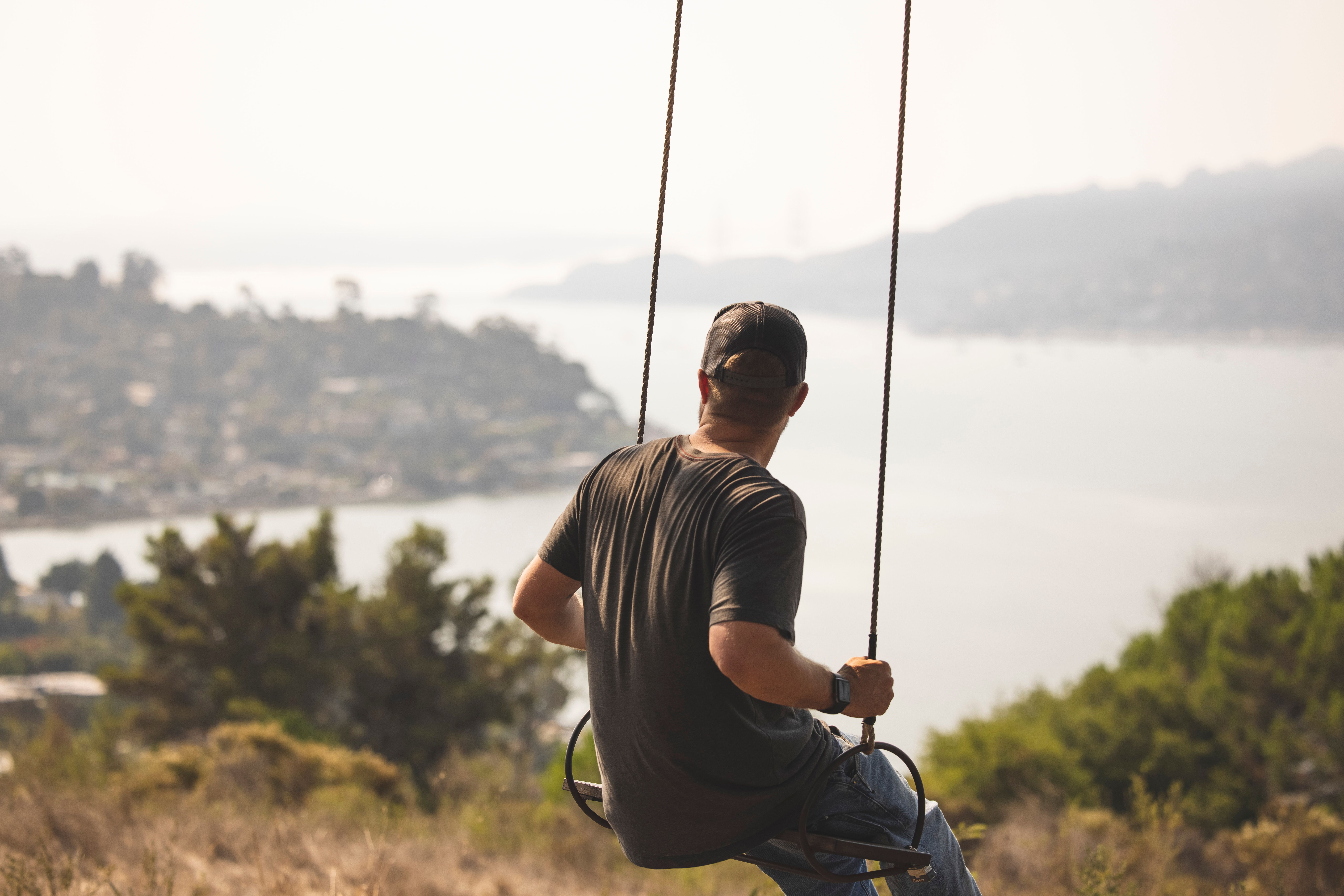 A man enjoying a swing with a breathtaking view of the coastline and distant cityscape.