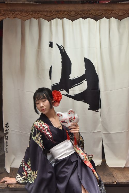 Free Young woman in kimono with fox mask against a backdrop of kanji curtains, exuding traditional Japanese elegance. Stock Photo