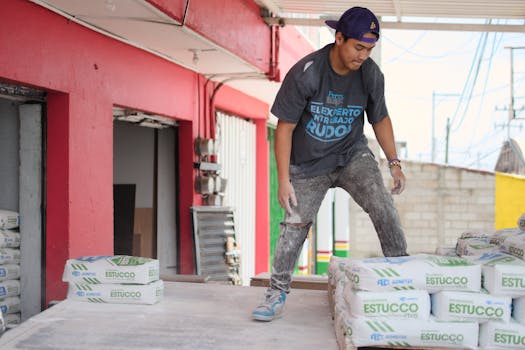 Young male construction worker unloading stucco bags at a job site.