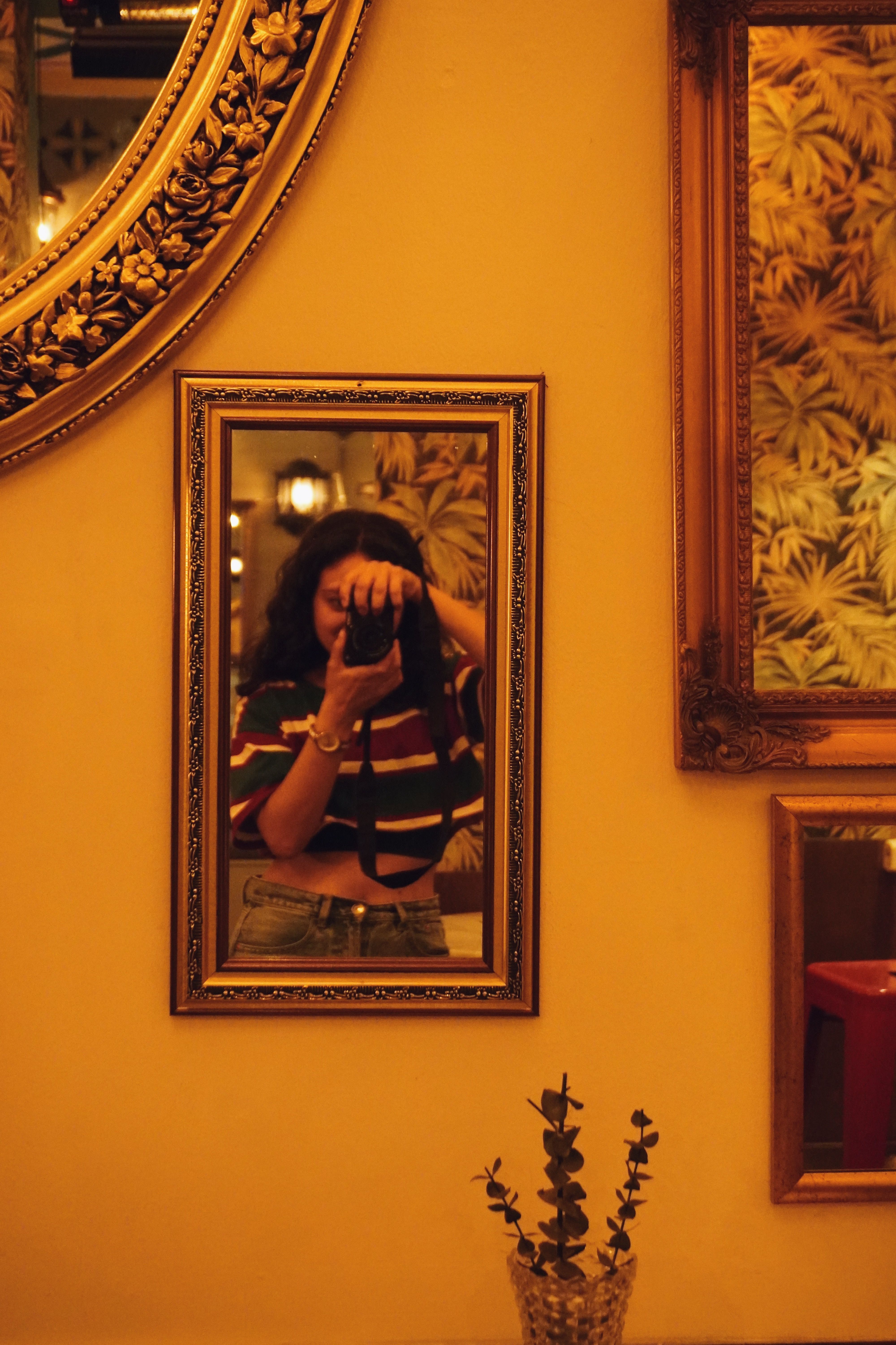A woman photographs herself in a framed mirror with warm cafe decor and reflections.