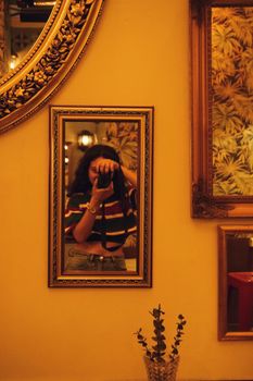 A woman photographs herself in a framed mirror with warm cafe decor and reflections.