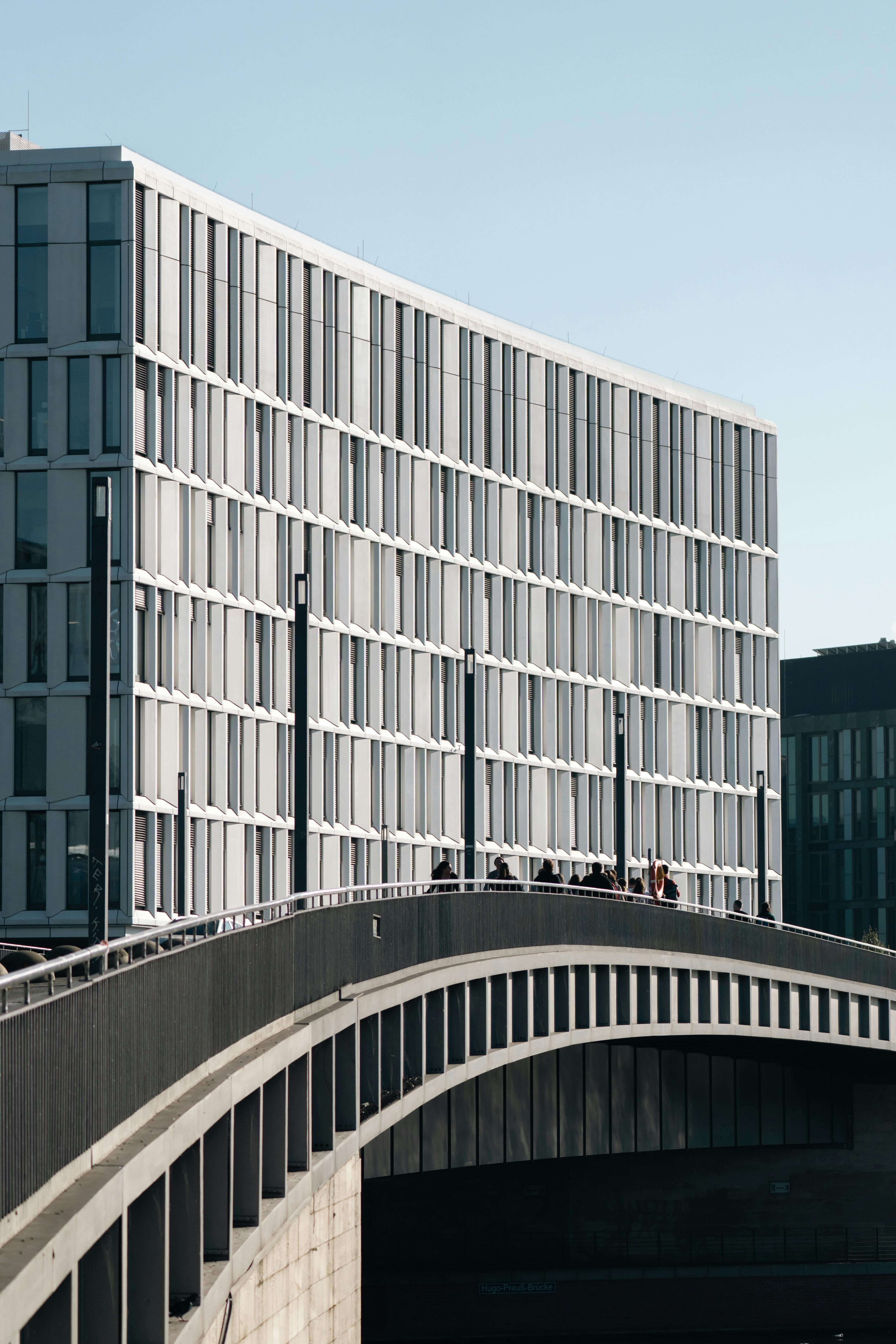 Contemporary building facade with arched bridge in urban setting, daylight view.