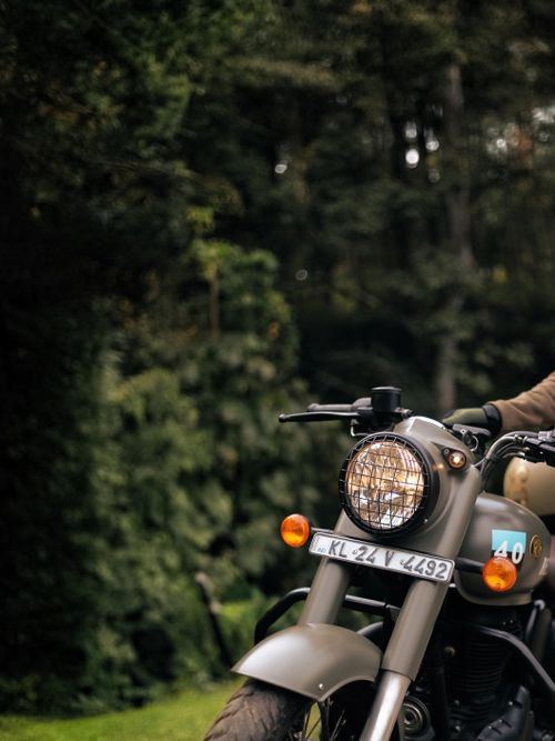 Free A classic motorcycle parked amidst greenery in Kerala's lush outdoors, representing adventure. Stock Photo
