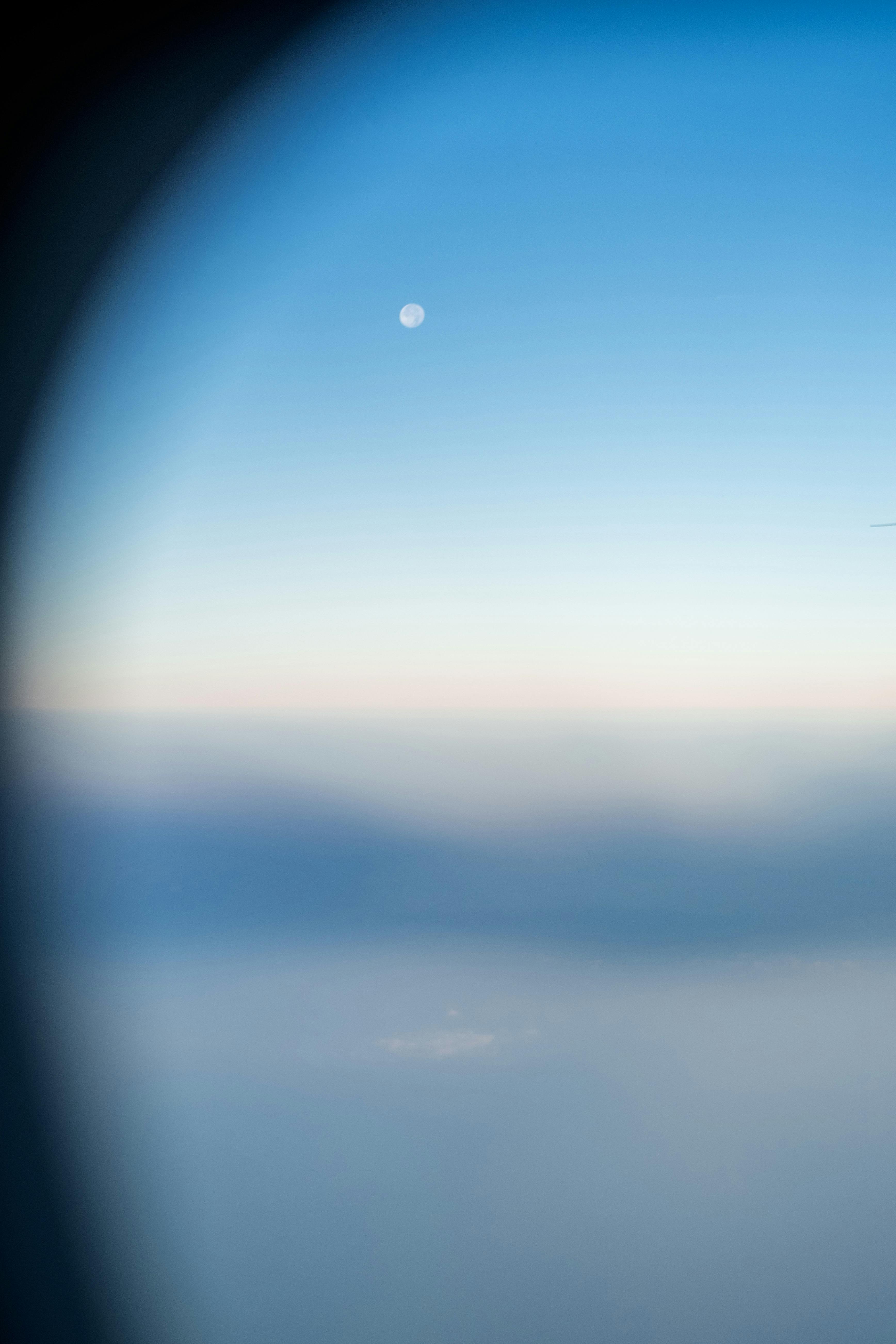 Moon visible through airplane window against a gradient sky. Captivating aerial view.