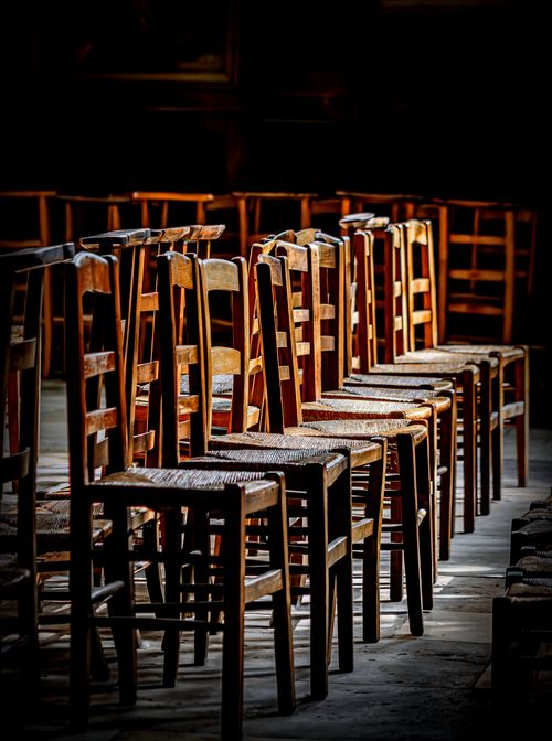 Free A series of wooden chairs neatly arranged in a dimly lit indoor setting with dramatic shadows. Stock Photo