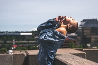 一位优雅的秃头妇女模型穿着牛仔夹克，站在有城市背景的屋顶上