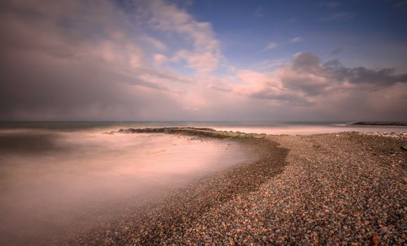 A tranquil evening scene of a pebble beach with gentle waves and a pastel sky.