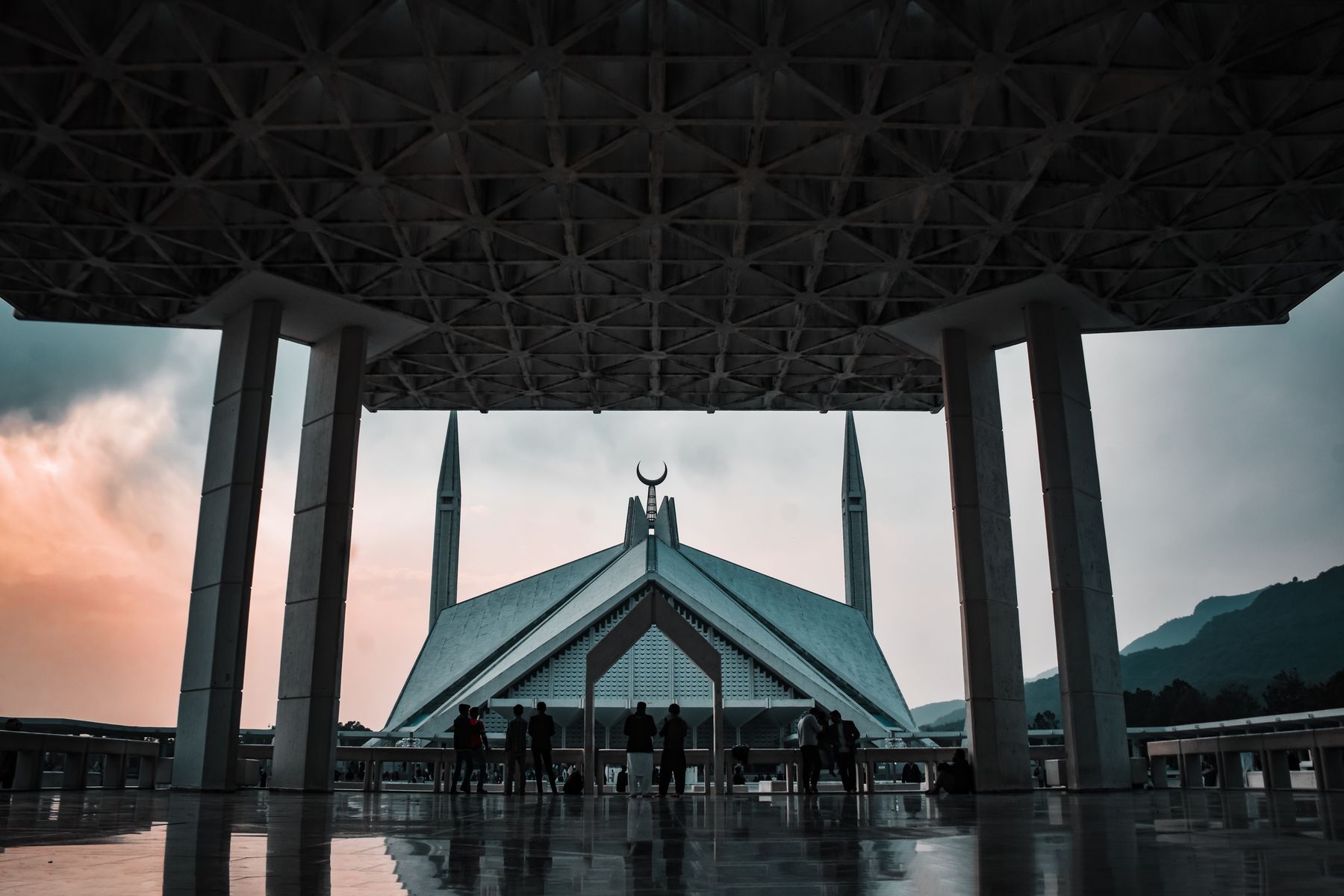 A stunning view of Faisal Mosque during twilight in Islamabad, showcasing Islamic architecture with silhouetted visitors.