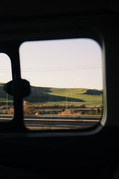 A serene view of rolling hills captured through a car window, showcasing lush greenery.