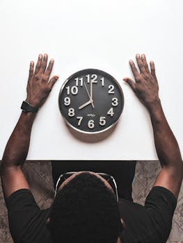 High angle view of a man with an apple watch observing a clock on a white table.