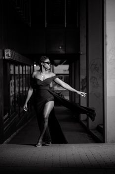 Stylish woman in a black gown walks gracefully in an indoor setting.